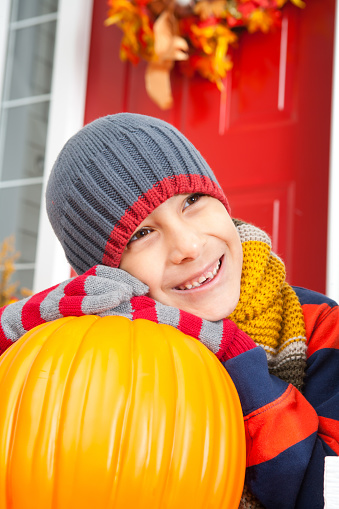 Smiling white boy holding big pumpkin sitting at front porch entrance
