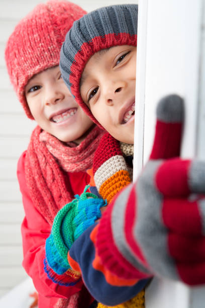 Two boys in red and yellow knit hat standing together near pine tree, rear view
