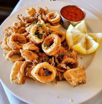Plate of golden delicious fried calamari rings and tentacles with a side of lemon and coctail sauce.