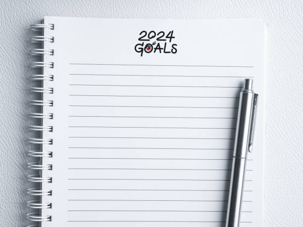 istock Goal, action and plan, resolution concept in new year 2024. Text, 2024 GOALS, handwriting with target dart icon and silver pen on template white blank paper for note on spiral notepad, top view. 1688193646
