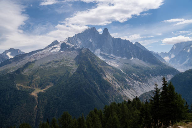 Woman wearing a backpack and cap, hiking with poles on rocky mountain path. Stunning alpine scenery and clear sky in the background. Outdoor adventure and nature exploration.