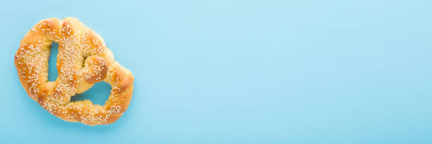 Soft pretzel with sesame seeds on light blue table background. Pastel color. Closeup. Wide banner. Empty place for text. Top down view.