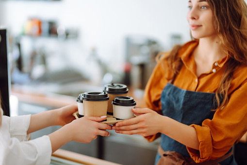 Close-up of a female barista's hands giving out a to-go drink order. The coffee shop owner gives orders to go. Takeaway drinks concept, small business.