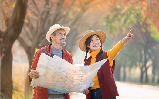 A senior man holding paper map talking with young adult daughter while she is pointing index to the location direction,happy moment of father and daughter spend holiday time in autumn travel together
