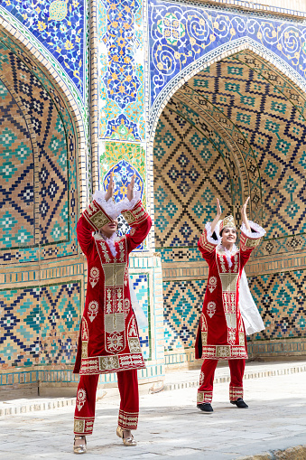 Folk show at public space. Young Uzbek women dancers, red national clothes, historical building at background. Travelling, national culture, entertainment concept. April 20, 2023 - Bukhara, Uzbekistan