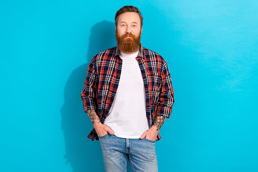 Photo of cheerful attractive guy wear checkered shirt arms hands pockets isolated blue color background.