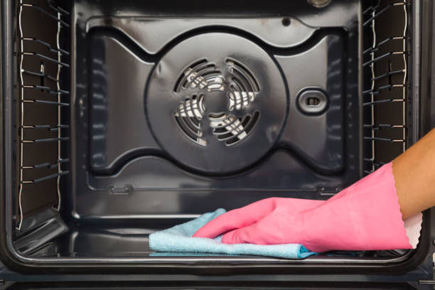 istock Woman hand in pink rubber protective glove using blue dry rag and wiping inside dark black oven at home kitchen. Closeup. Front view. Regular cleanup. 1688254673