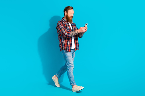 Full length size photo of satisfied red hair man walking texting coworkers while street rest going isolated on blue color background.