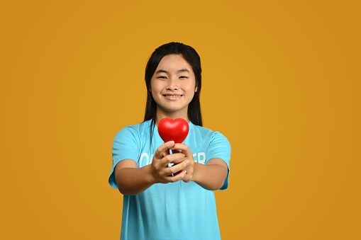 Teenager asian girl wearing volunteer t-shirt isolated on yellow background. Charity, support, altruism and donation concept.