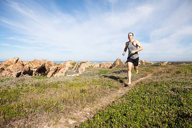 Male athlete running barefoot and fast on a walking trail close to the sea.