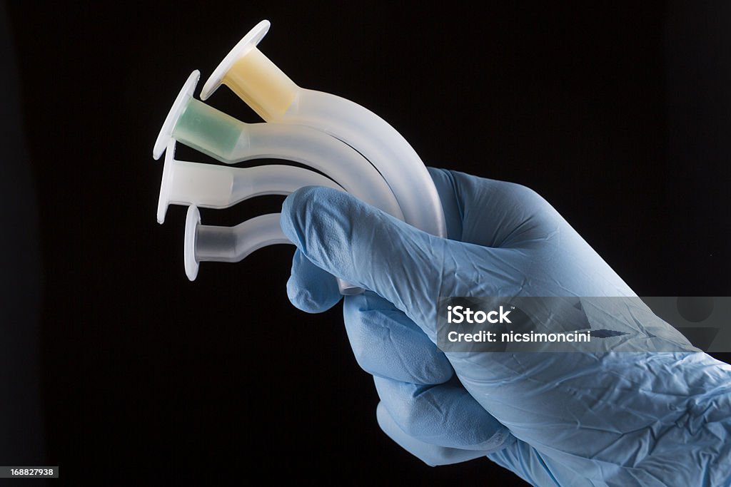 Oropharyngeal Airways in a hand A hand in a surgical glove holding four oropharyngeal airways , isolated on black Respiratory Tract Stock Photo