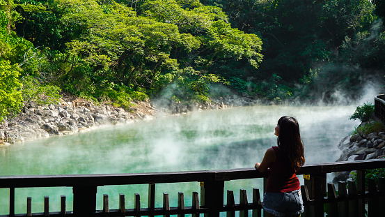 Hot steam at thermal valley, Beitou, Taipei, Taiwan. Woman traveler looking at Hot spring pond at Xinbeitou thermal valley in Taiwan.