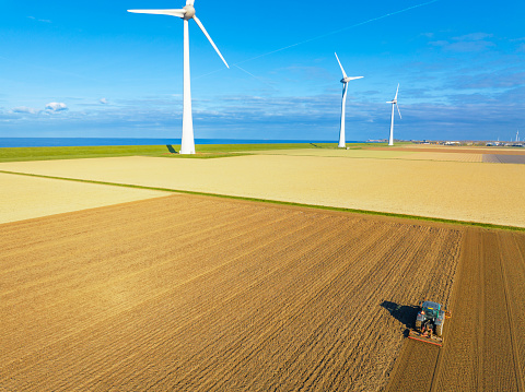 Tractor cultivating the soil during springtime seen from above with wind turbines in the background during a sunny and dry springtime day. Aerial view drone view from directly above.