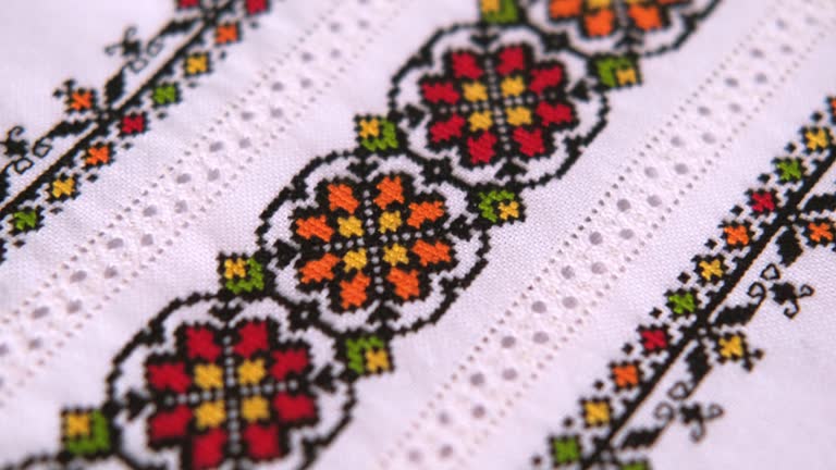 Texture of linen white fabric with an embroidered element. Cross stitches with colored threads and artfully made hemstitching. Ukrainian embroidery pattern for folk shirt.