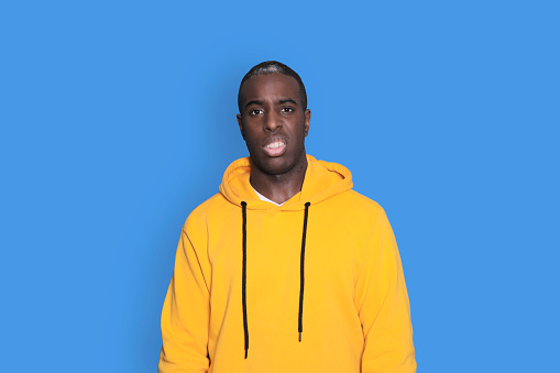 Young sad frustrated worried man in yellow hoodie looking camera isolated on blue wall background studio portrait. People sincere emotions lifestyle concept. Mock up copy space