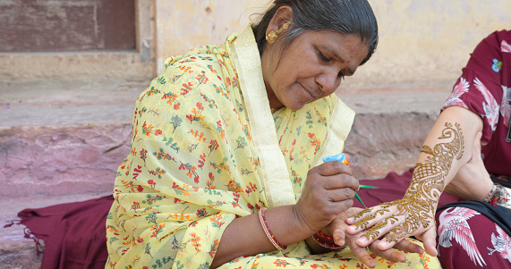 Indian woman making henna painting on a tourist hand in Jaipur. Jaipur is known as the Pink City, because of the color of the stone exclusively used for the construction of all the structures.