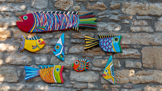 Gokceada, Canakkale, Turkey July 22, 2023 Colorful wooden fish ornaments on the stone wall in Ilıos Hotel. Modern Wood Art. Handmade carved from wood