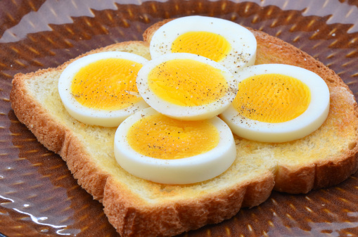 Hard boiled egg slices on white toast sprinkled with salt and pepper
