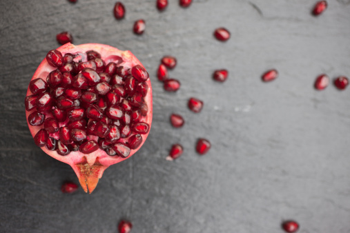 Fresh pomegranate juice in a glass and a lot of pomegranates on a gray concrete surface. Copy space.