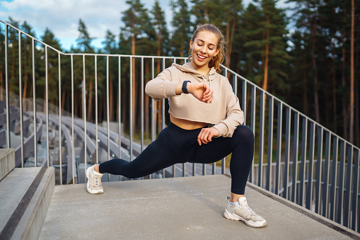 An active woman in sportswear does a stretching exercise, looks at a fitness application through a Smartwatch. Concept for sport, training or active lifestyle.