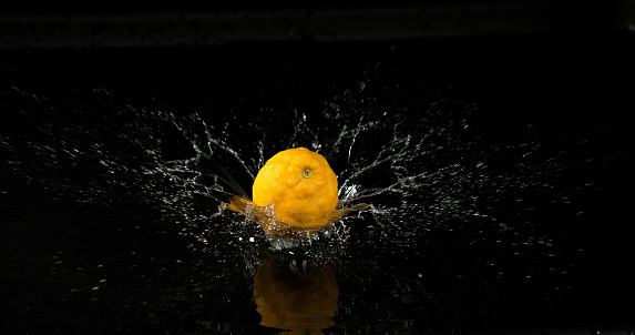 Three fresh juicy lemons falling into crystal clear water. There are splashes of water and bubbles rising high above the lemons from where they break the waters surface. The fruit and splashes are isolated on a white background.