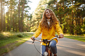 A smiling female tourist in a yellow coat enjoys the weather in the autumn park.