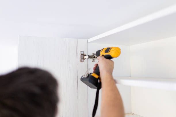 istock Carpenter holding electrical screwdriver to fix wooden door hinge. Kitchen unit installation concept. 1688427895
