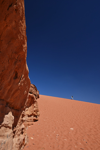 A solitary tourist walks down a red sand dune in the Wadi Rum desert.