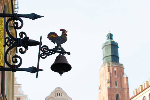 Metal bell with forged rooster and decorative elements on the facade and tower of an old building. Poland, Wroclaw, January 2023