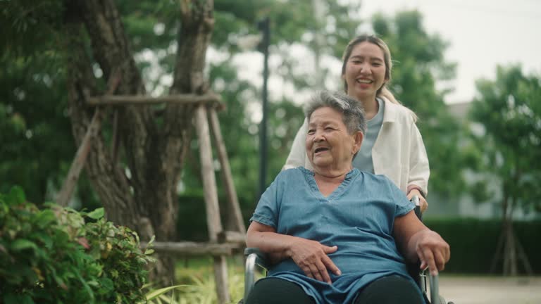 Asian teen woman taking care her grandma on wheelchair at park.