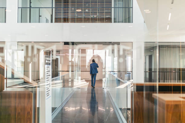 Individuals in a bustling modern office setting, actively working and interacting with laptops and documents. Large windows let in abundant natural light, creating a bright and energetic atmosphere, while some professionals move dynamically through the space, contributing to a vibrant work environment.