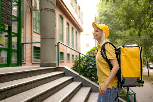 Happy female courier walking up the stairs towards the residential building.