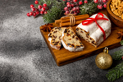 Christmas stollen - traditional German bread on a brown wooden table with fir branches. Festive dessert made of dough, nuts and marzipans sprinkled with powdered sugar.Copy space. Place for text.