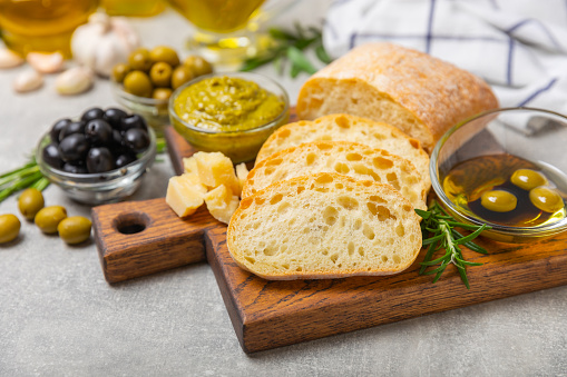 Italian ciabatta bread cut in slices with herbs, olives, pesto sauce, garlic and parmesan cheese on a concrete table. Fresh homemade Italian Ciabatta bread sliced with herbs and spices.Place for text.
