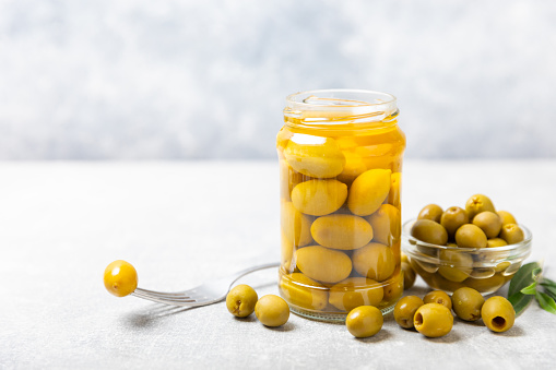 Olives in a glass jar on a concrete background. pitted  olives in jar.Pickled olives in glass jar. On a wooden background.Marinaded olives. Space for text.Space for copy. Vegan food.