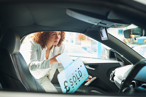 car saleswoman putting sold sign in car