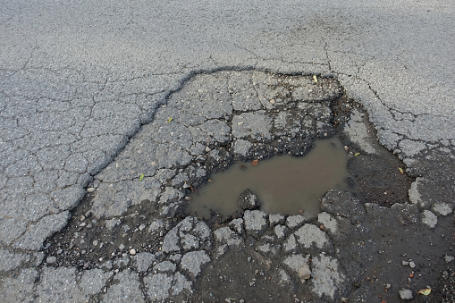 Pothole on cracked asphalt road filled with water