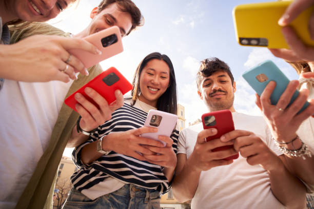 Low angle view multiracial group young generation z in circle using phones together outdoors. stock photo