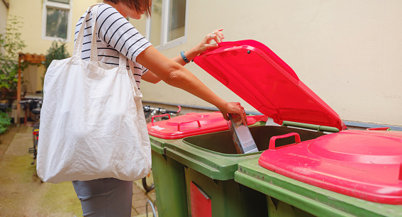 Recycling bins, Sorting and disposing, sustainable lifestyle concept. Asian Woman putting paper garbage to the recylcing bin which stands in the courtyard of her house