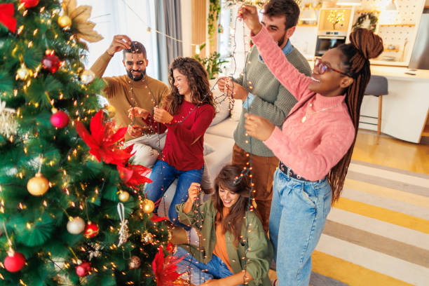 istock Friends placing Christmas lights on Christmas tree while decorating it 1688539385