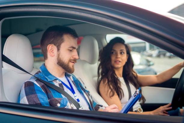 istock Cheerful pretty young lady sitting inside car with man instructor by her side, writing drive report. Test drive, transportation, safety, education concept 1688551977