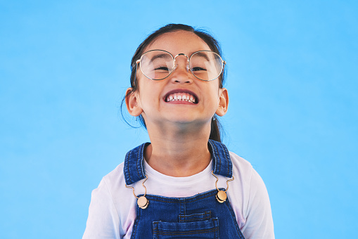 Glasses, student smile and Asian child in portrait in studio isolated on a blue background mockup space. Happy, nerd and face of school kid, girl or geek in casual clothes, fashion and style in Japan