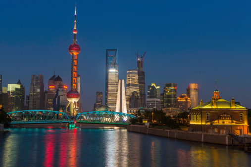 The iconic spire of the Oriental Pearl Tower and futuristic skyscrapers of Shanghai's Pudong financial district overlooking the historic trusses of Waibaidu Bridge under clear blue dusk skies, China. ProPhoto RGB profile for maximum color fidelity and gamut.