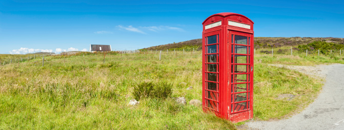 Iconic British red phone box in picturesque rural landscape under clear blue panoramic summer skies. ProPhoto RGB color profile for maximum color gamut.