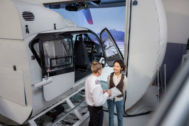 High angle view of instructor pilot giving training to female student standing by helicopter flight simulator at a aviation academy. Pilot teaching to a woman student at flying school.