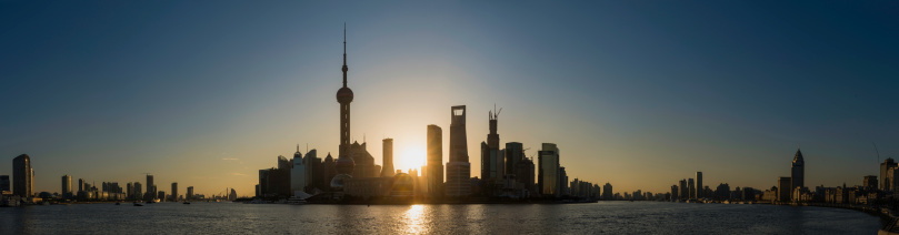 Dramatic sunburst and rays of light silhouetting the futuristic skyline of Pudong at daybreak with the iconic spire of the Oriental Pearl Tower and skyscrapers of the Lujiazui financial district reaching into the blue summer skies of Shanghai above the Huangpu River, China. ProPhoto RGB profile for maximum color fidelity and gamut.