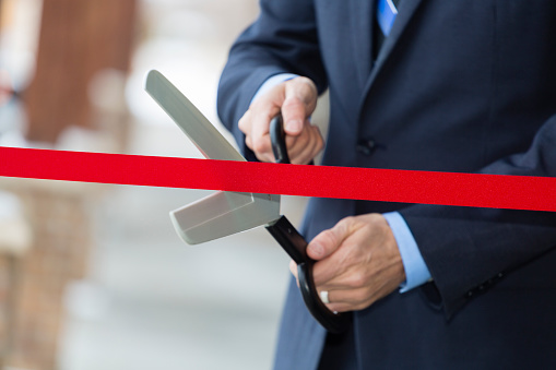 A ceremonial ribbon cutting with large scissors in front of a business.