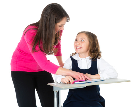 A teacher helping a student sitting at a classroom desk.  Isolated on a white background.