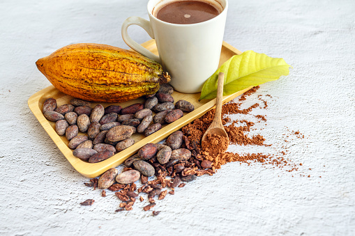 Cocoa powder and beans with cocoa drink on a wooden serving tray, cocoa nibs, and cacao leaves.