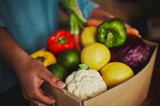 An unidentifiable person holding a box of fresh fruit and vegetables